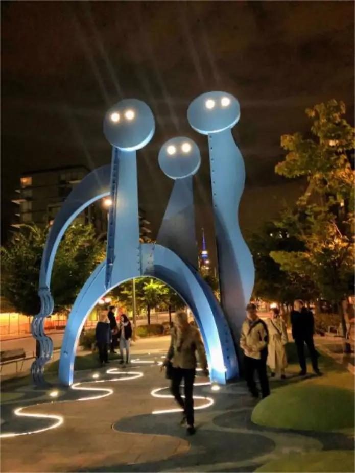 Des passants sous une sculpture géante. Archives 2019 West Don Lands.