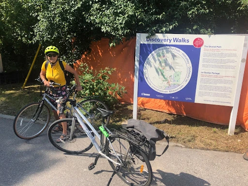 Rolande, une guide la SHT, à vélo, près de l'affiche Discovery Walks.